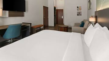Une chambre d’hôtel comprenant un lit, un bureau avec une chaise, une petite table ronde, un canapé et un téléviseur fixé au mur.