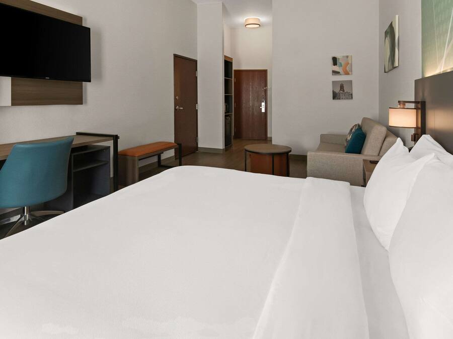 Une chambre d’hôtel comprenant un lit, un bureau avec une chaise, une petite table ronde, un canapé et un téléviseur fixé au mur.