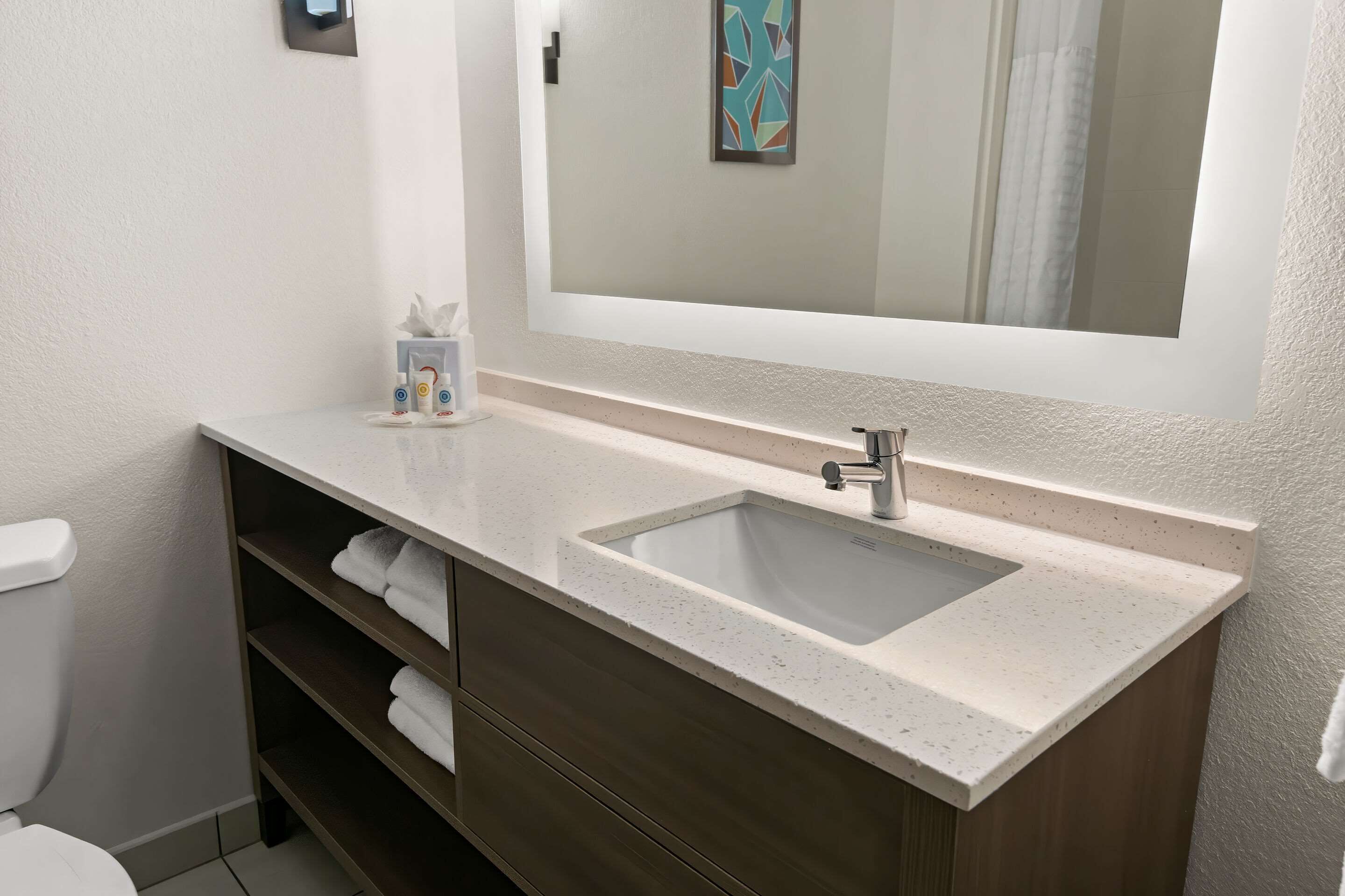 Un baño con un lavamanos blanco, un espejo y un perchero para toallas.