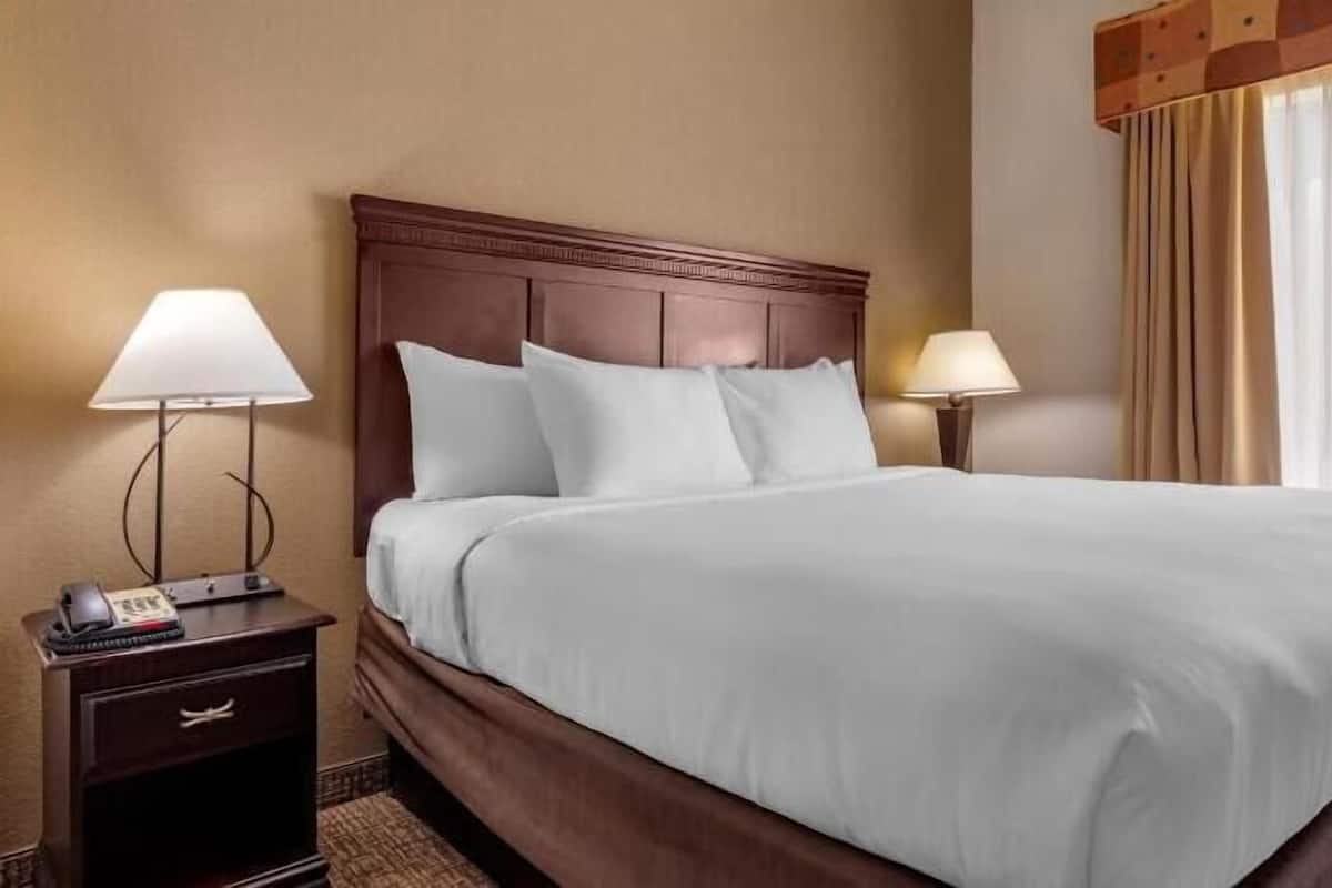 A hotel room with a large bed, two bedside lamps, a telephone, and a window with curtains.