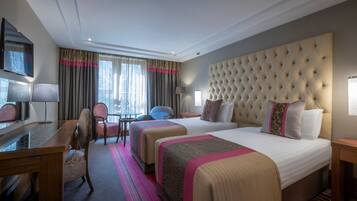 A hotel room with a large bed, a desk, a chair, and a TV.