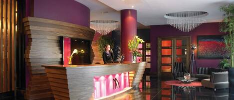 A modern reception area with a wooden reception desk, a large chandelier, and a red carpet.