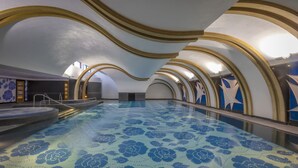 A swimming pool with a blue floral pattern on the floor, surrounded by arched ceilings with gold trim.