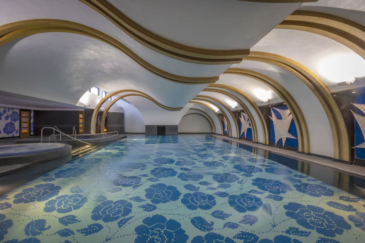 A swimming pool with a blue floral pattern on the floor, surrounded by arched ceilings with gold trim.