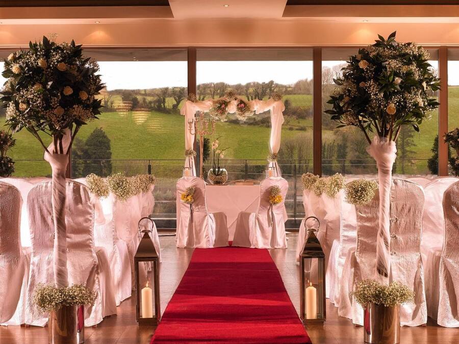 A wedding ceremony setup with a red carpet, white chairs, and floral arrangements.