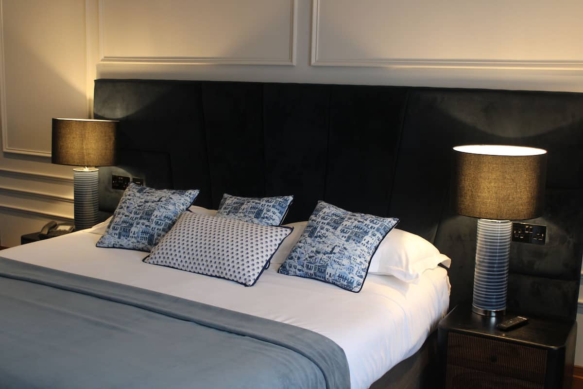 A neatly made bed with a dark headboard, two bedside lamps, and patterned pillows.