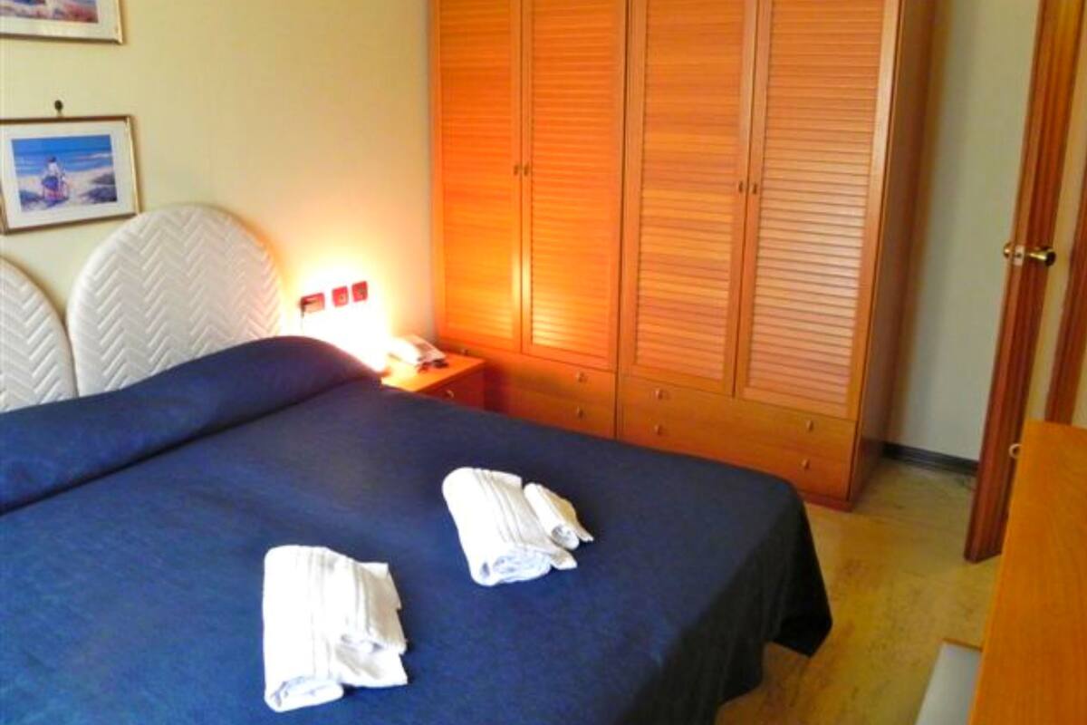 A hotel room with a bed, a nightstand, a lamp, and a wardrobe.