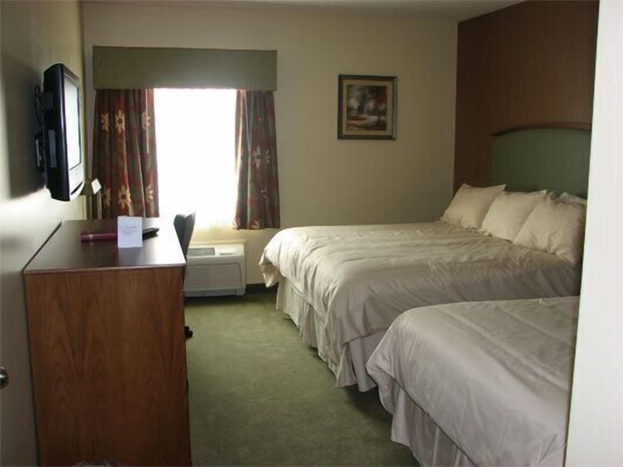A hotel room with two beds, a desk, a television, and a window with curtains.