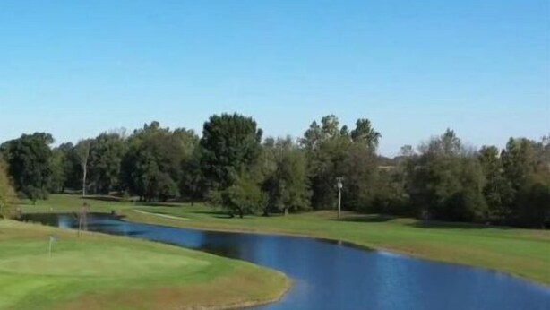A golf course with a pond, trees, and a clear sky. - Randolph Inn and Suites (Winchester)