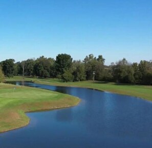 A golf course with a pond, trees, and a clear sky. - Randolph Inn and Suites (Winchester)