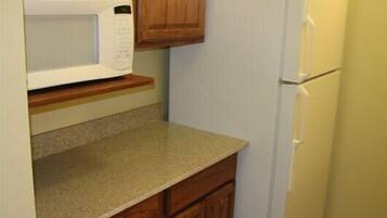 A kitchen with a microwave, a refrigerator, wooden cabinets, and a granite countertop.