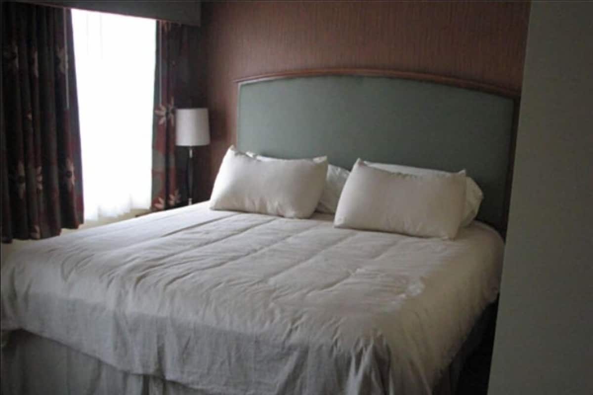 A hotel room with a large bed, a headboard, and a window with curtains.