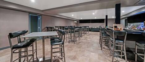 A modern dining area with high tables and metal chairs, a bar with stools, and a tiled floor.
