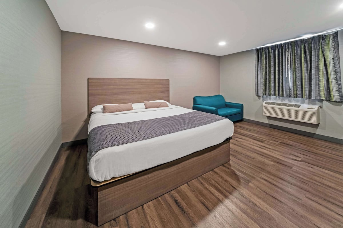 A modern bedroom with a large bed, a blue armchair, and a window with curtains.