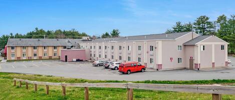 A multi-story motel with a parking lot, several cars parked, and a red van in the foreground.