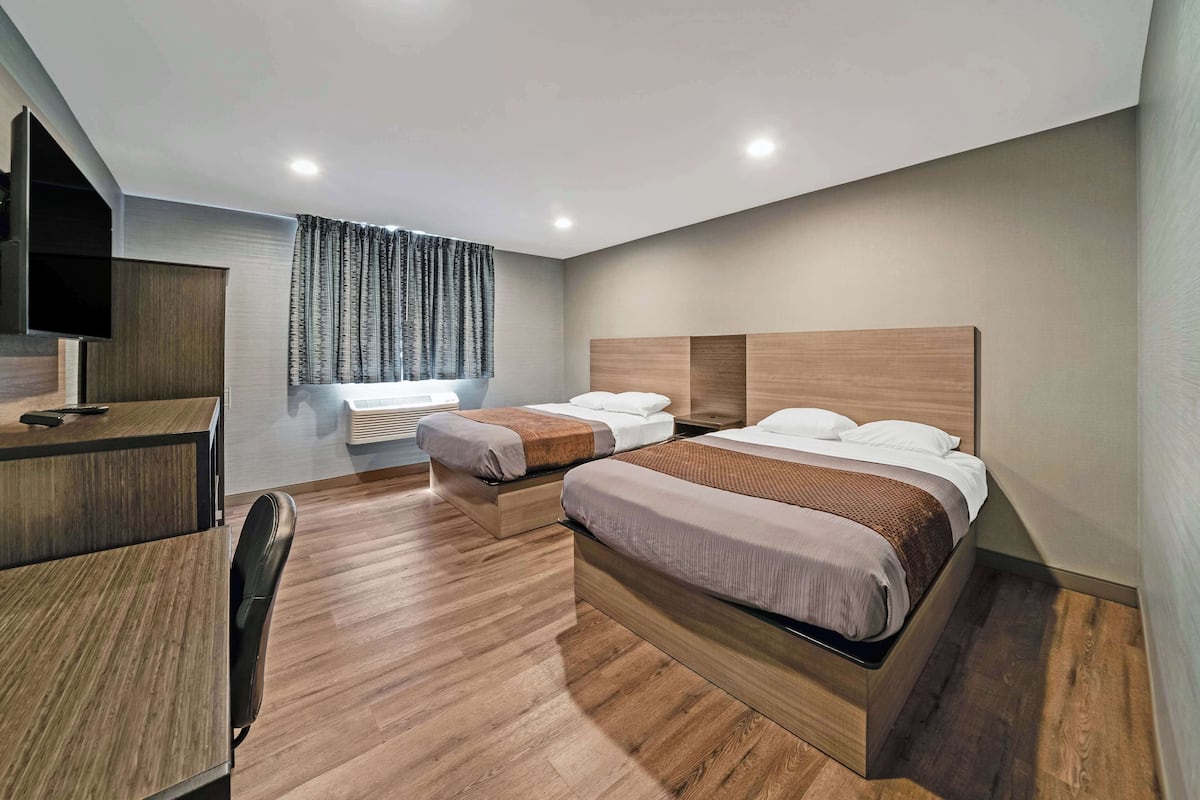 A modern hotel room with two beds, a desk, and a TV.