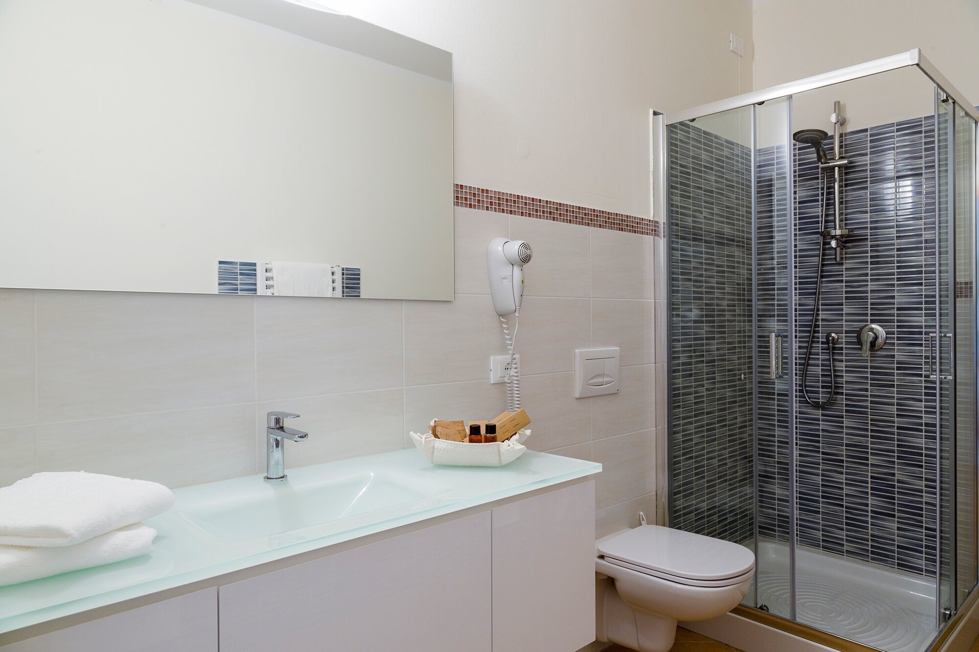 A bathroom with a glass shower enclosure, a white sink, and a toilet.