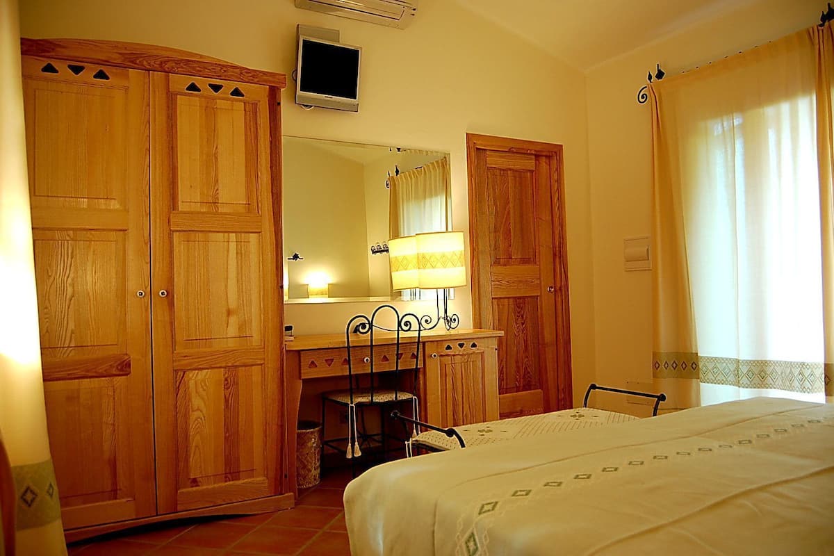 A bedroom with wooden wardrobes, a bedside table, a chair, a bed, a mirror, and a TV.