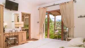 Une chambre à coucher avec un lit, une coiffeuse avec un miroir, une télévision et une vue sur la verdure à l’extérieur.