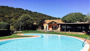Une piscine à bord incurvé, un bâtiment avec un toit en tuiles et un paysage vallonné en arrière-plan.