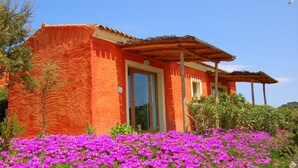 Un bâtiment à l’extérieur rouge, doté d’un porche abrité, entouré d’un champ de fleurs violettes.