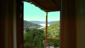 Un balcon doté de meubles en osier, offrant une vue sur une vallée verdoyante et un lac.