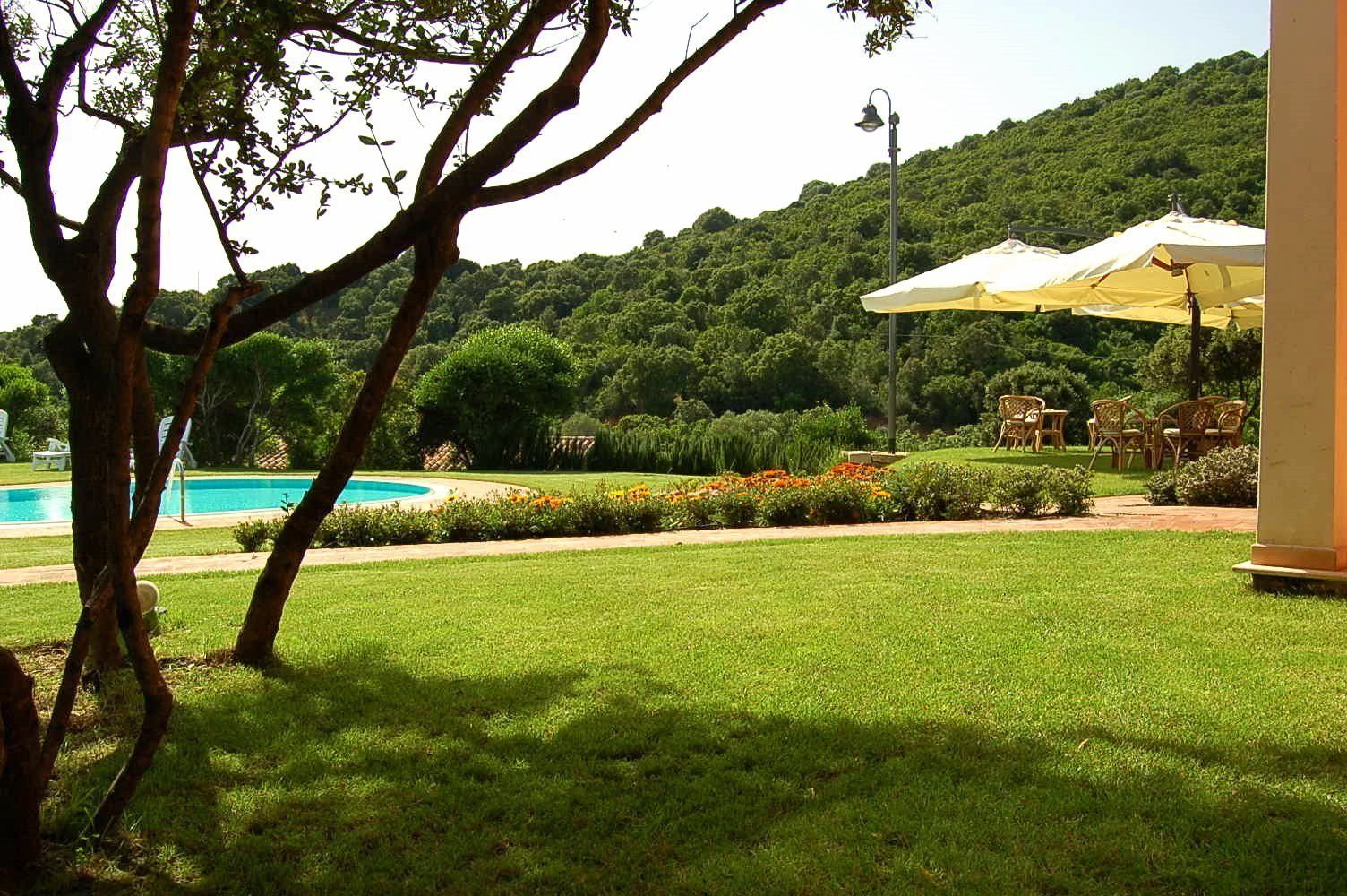 Ein Pool, umgeben von einer gepflegten Rasenfläche, Gartenmöbeln und einem Hügel mit dichter Vegetation im Hintergrund.