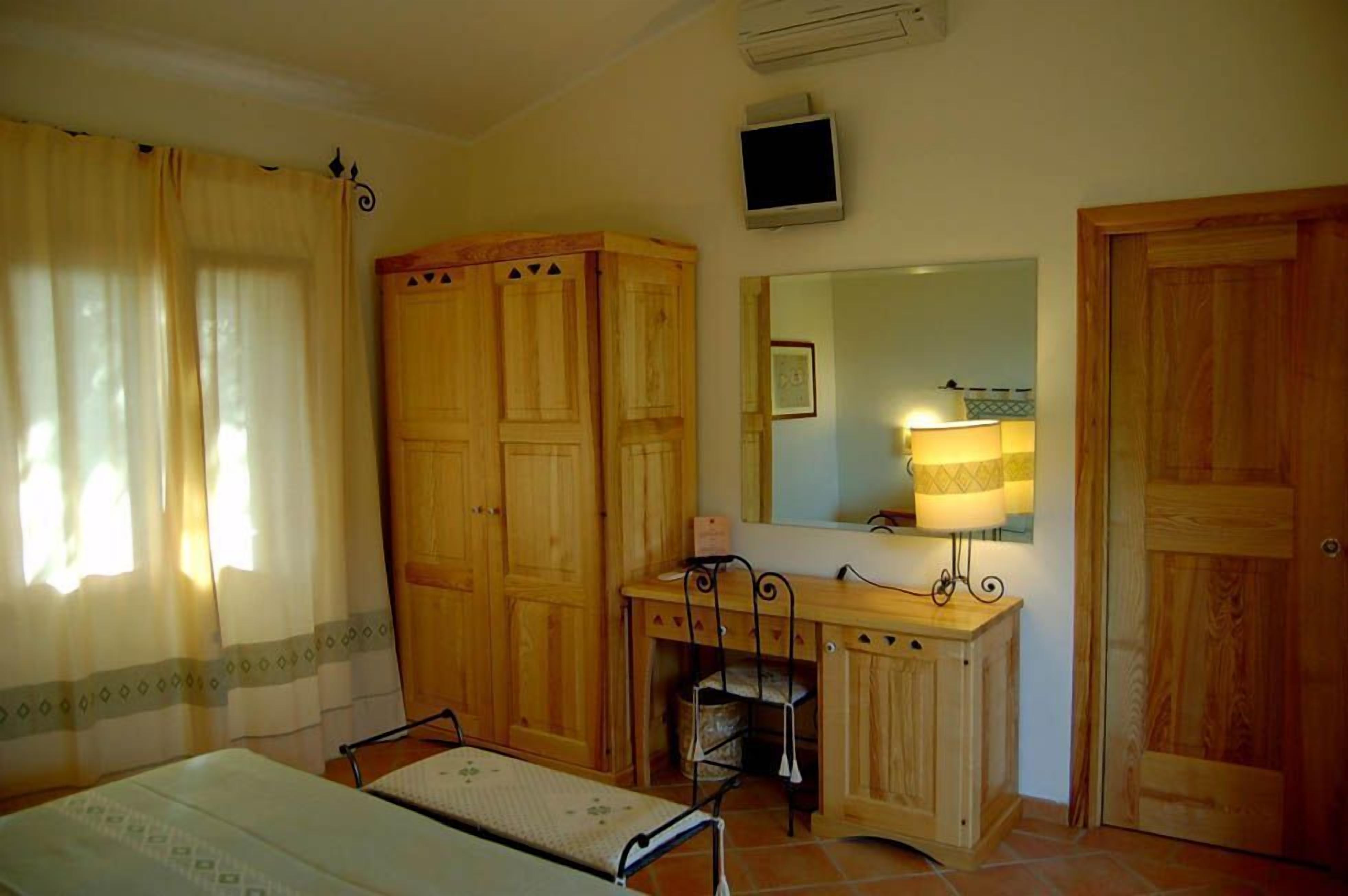 Een kamer met een bed, een bureau, een stoel, een kledingkast, een spiegel en een televisie.