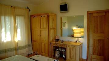 Een kamer met een bed, een bureau, een stoel, een kledingkast, een spiegel en een televisie.