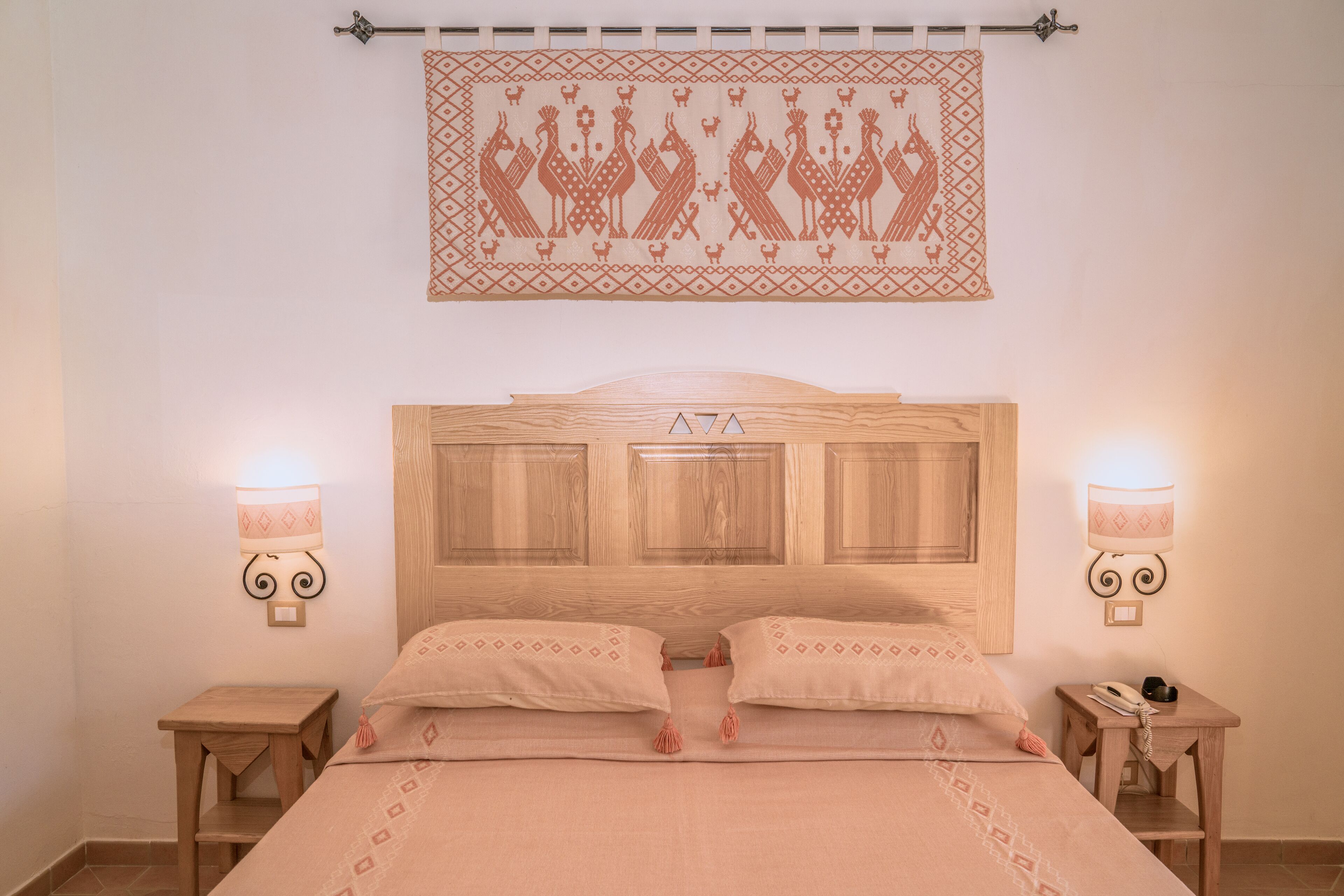 Quarto bem arrumado com cabeceira de madeira, duas mesas de cabeceira com luminárias e uma tapeçaria estampada acima da cama.