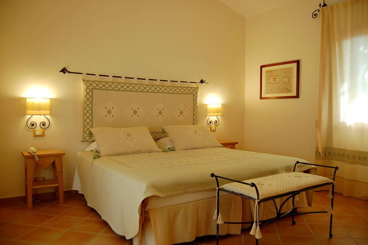 A neatly arranged bedroom with a bed, bedside lamps, a bedside table, a chair, and a framed map on the wall.