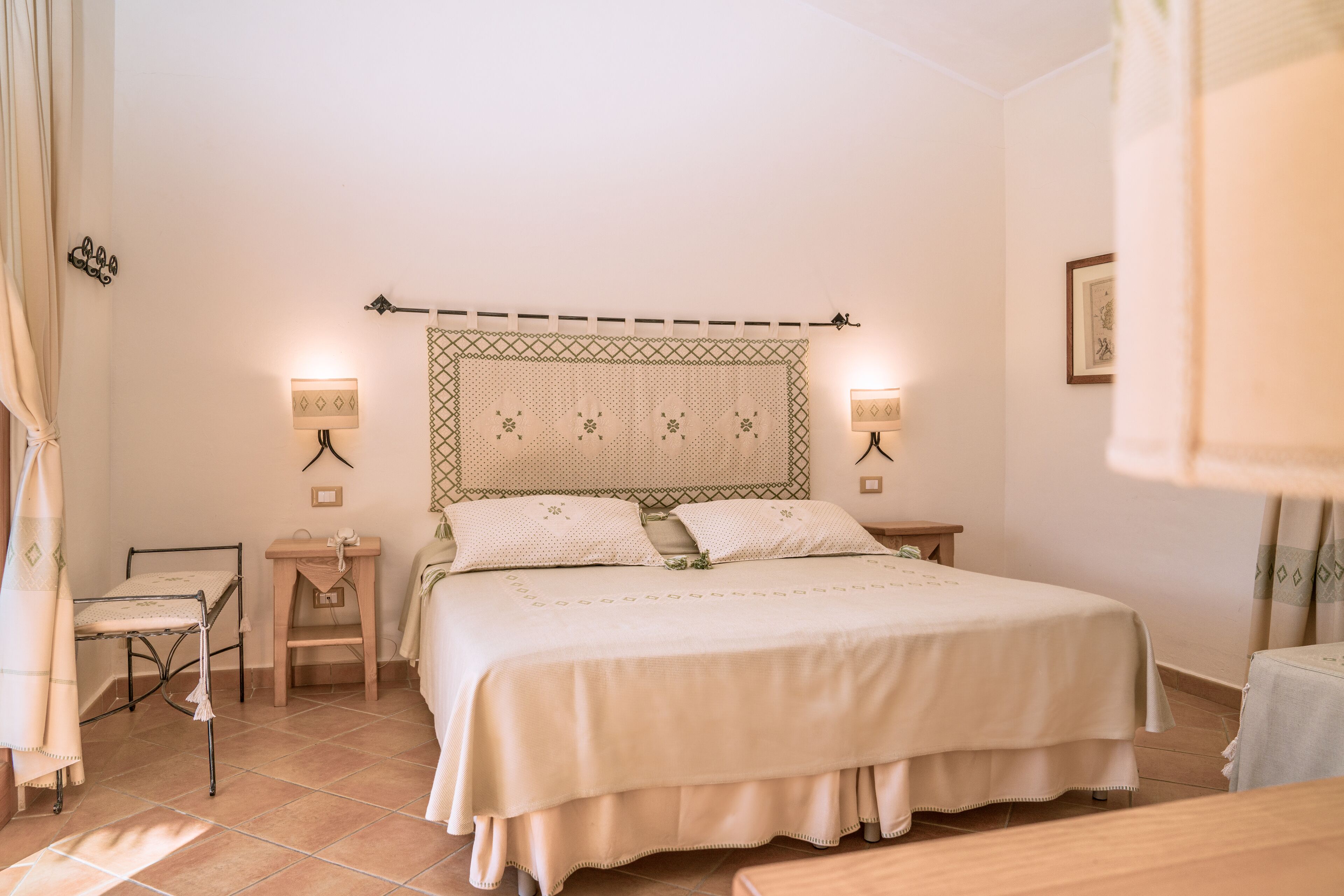 Quarto bem arrumado com cama, mesas de cabeceira e uma cadeira.