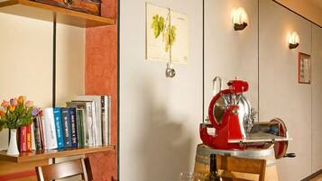 Uma área de refeições com uma mesa posta para dois, uma estante de livros e uma máquina de café expresso vermelha.