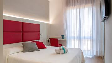 Una habitación de hotel moderna con una cama grande, cabecera roja y un escritorio con silla.