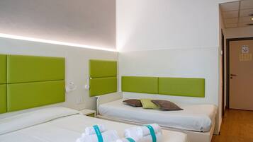 Una camera d'albergo con due letti, ciascuno con una testiera verde, biancheria bianca e un paio di asciugamani con un nastro color acquamarina.