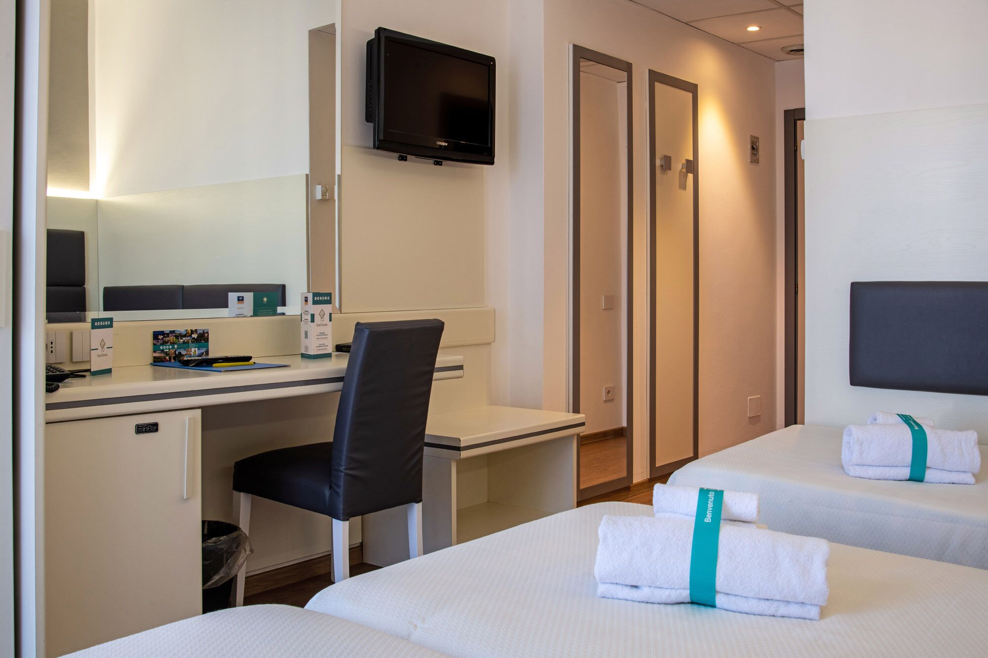 Habitación de hotel con dos camas, un escritorio, una silla, un televisor y un mini bar.