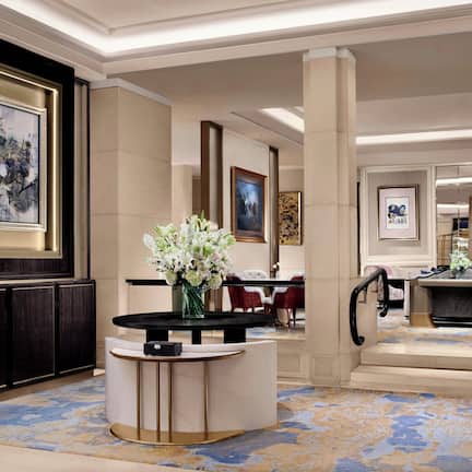 A hotel lobby with a marble floor, a reception desk, a large framed abstract painting, and a vase of flowers.
