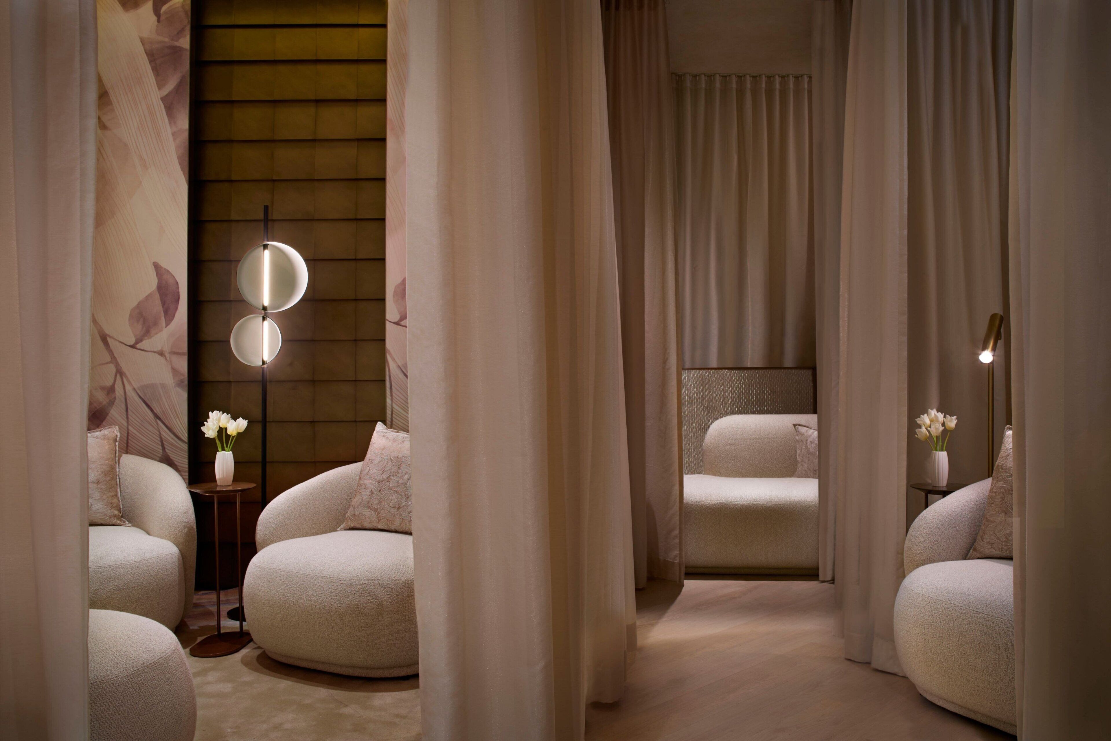 A spa room with two sofas, a small table with a vase of flowers, and a wall with a floral pattern.