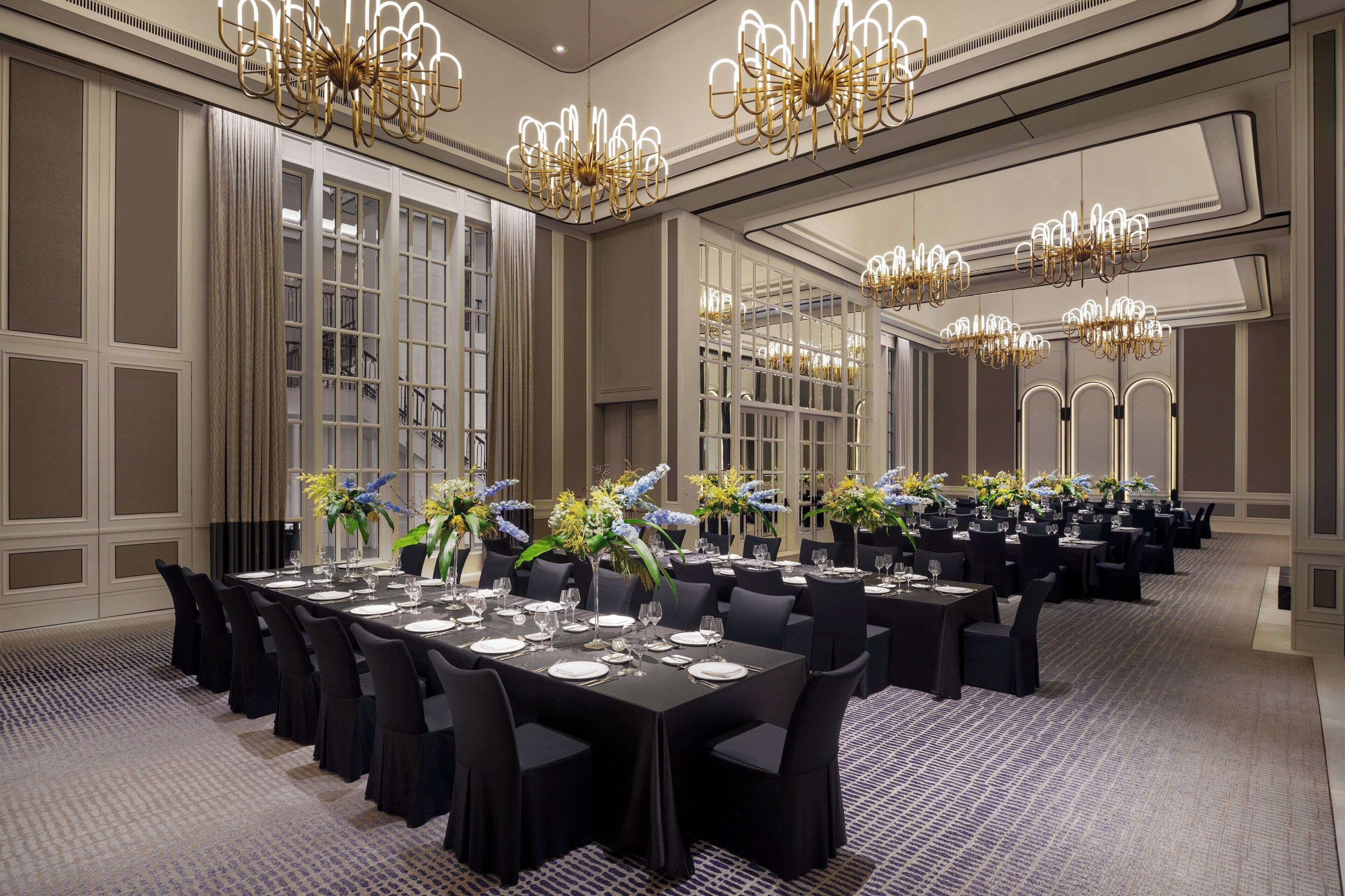 Un salón de banquetes con varias mesas redondas, sillas negras y candelabros.