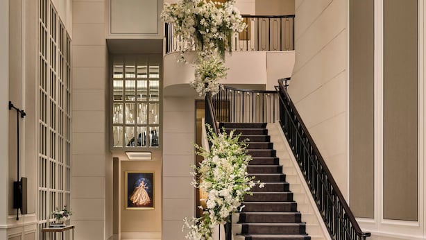A grand staircase with a black railing, flanked by white walls and a large window.