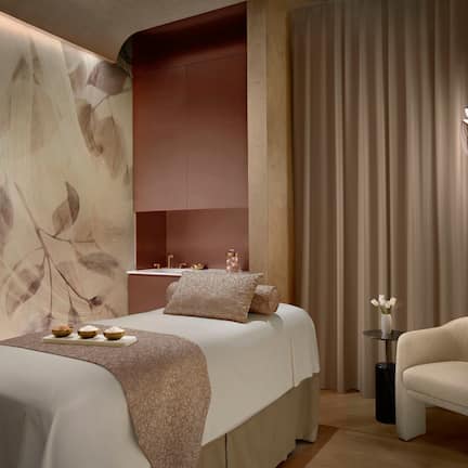 A modern bedroom with a large bed, a side table with a vase, and a chair.