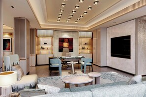 A modern hotel lobby with a central seating area, a large TV screen, and a patterned carpet.