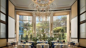 A spacious dining area with large windows, a chandelier, and multiple tables and chairs.