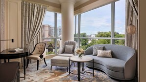 A modern hotel room with a large window, a grey sofa, a matching armchair, a small table, and a decorative vase.