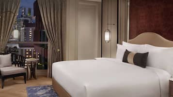 A hotel room with a large bed, a chair, a small table, and a view of a cityscape at night.
