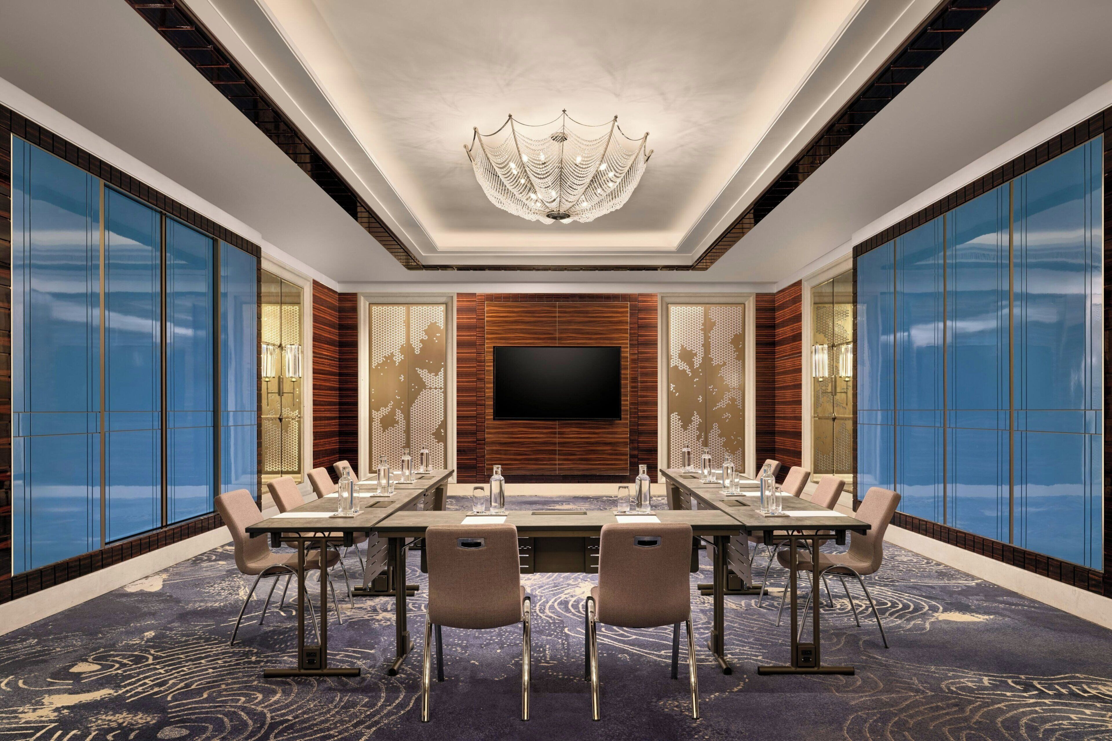 A conference room with a large flat-screen TV, a chandelier, and a patterned carpet.