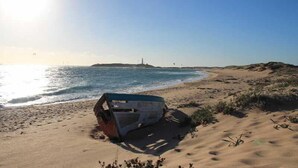 Una playa arenosa con un bote en la orilla y un faro a lo lejos.