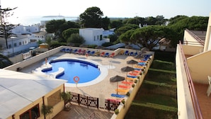 Una piscina en la azotea con vista al mar, rodeada de sillones y sombrillas.