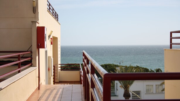 Un balcón con vista al mar, suelo de baldosas y barandilla roja.