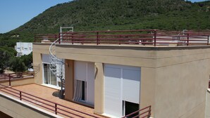 Un edificio moderno con terraza en la azotea, ventanas amplias y vistas a una colina verde.